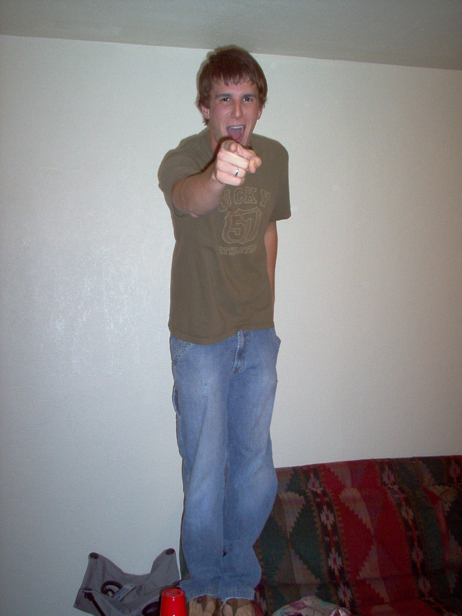 lex Kanzler pointing in a room with a plain wall and colorful rug.