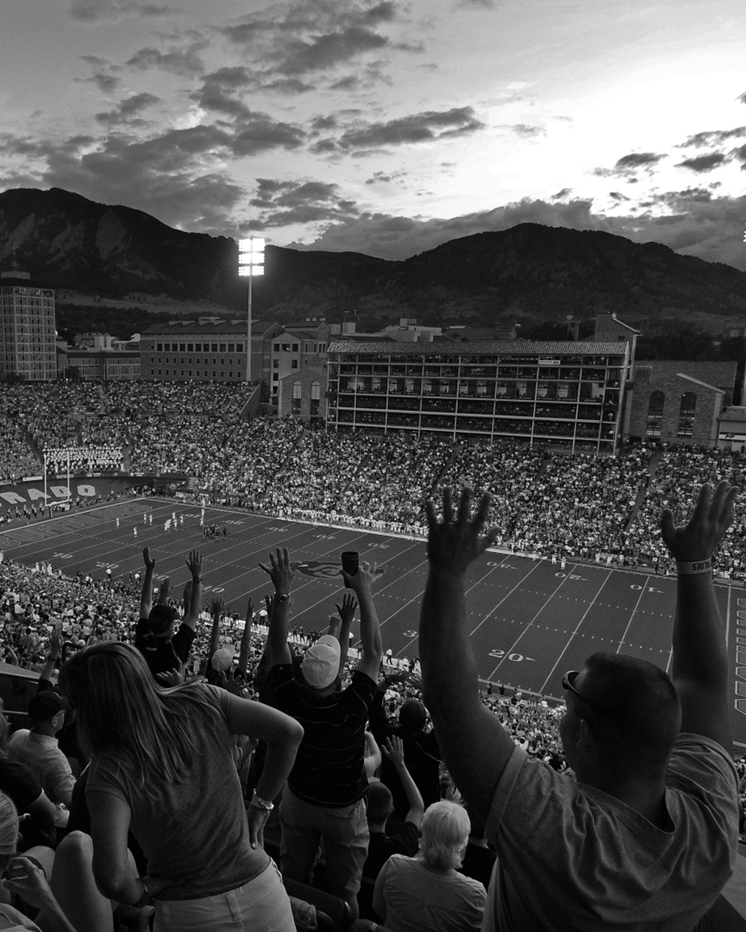People in a stadium with arms raised, likely at a sports event, with mountains in the background.